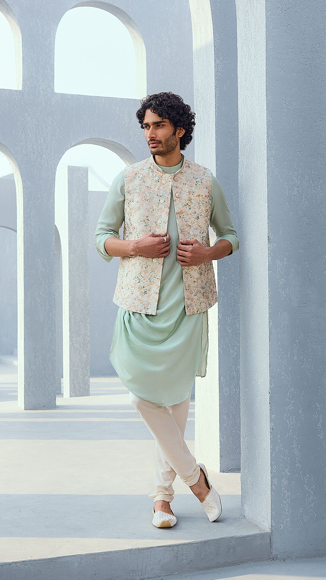Man wearing a pastel green kurta set with a floral Nehru jacket in an architectural outdoor setting